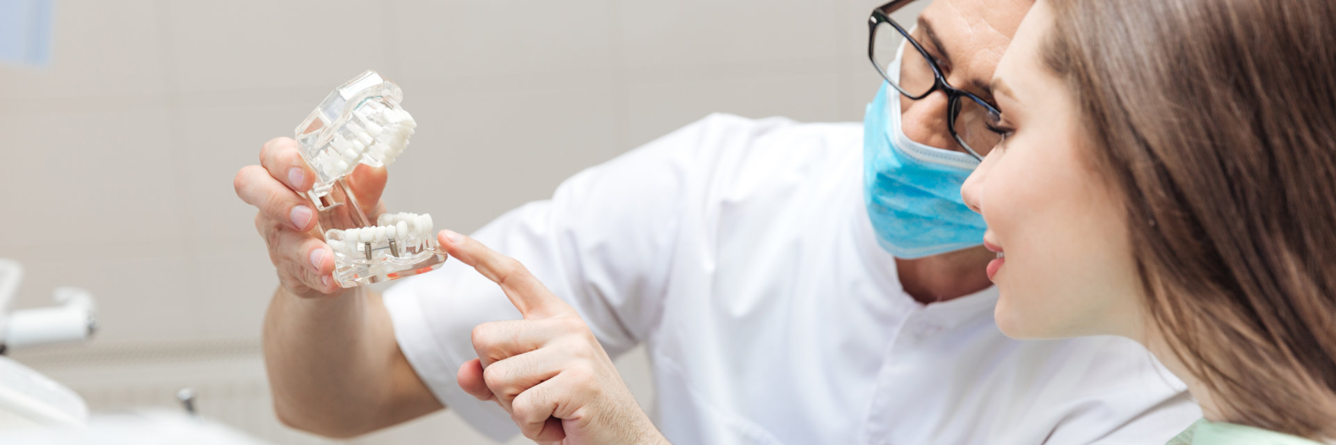 A dentist with a dental model explaining dental implants treatment to a woman patient.