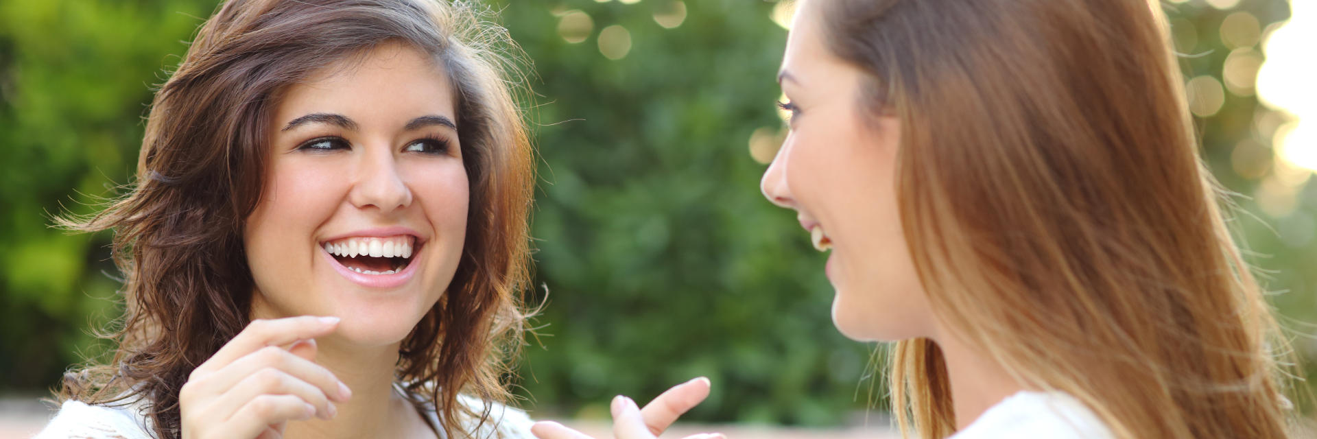 Two cheerful young women with perfect smiles chatting in the park.