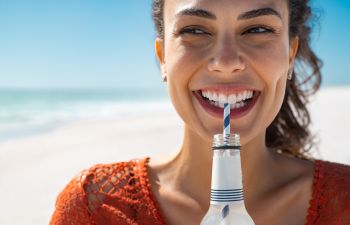beautiful young woman with a perfect smile drinking water through a straw.